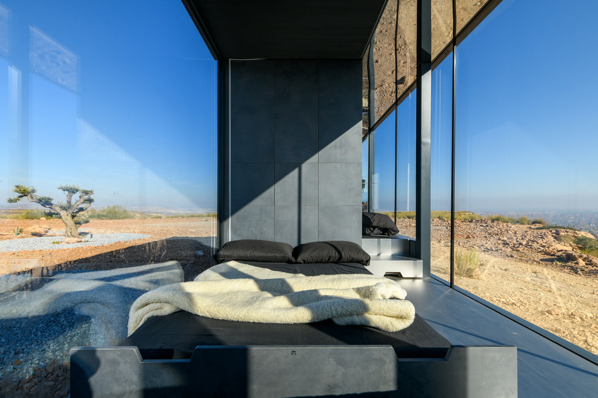 Blick in das Schlafzimmer einer Ferienwohnung. Die Wände rechts und links bestehen aus großen Fenstern